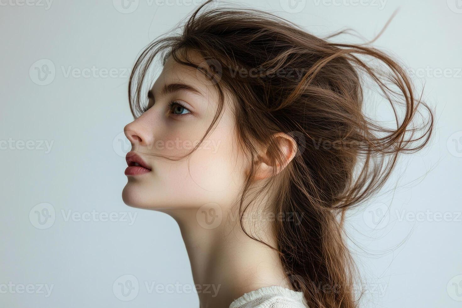 Profile shot of a beautiful young brunette with wind-swept hair against a white backdrop. photo