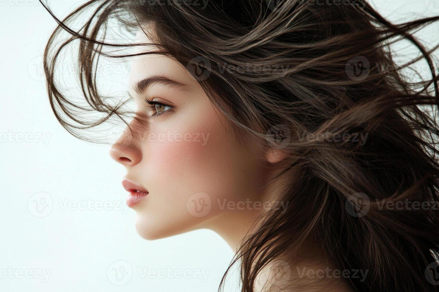 Profile shot of a beautiful young brunette with wind-swept hair against a white backdrop. photo