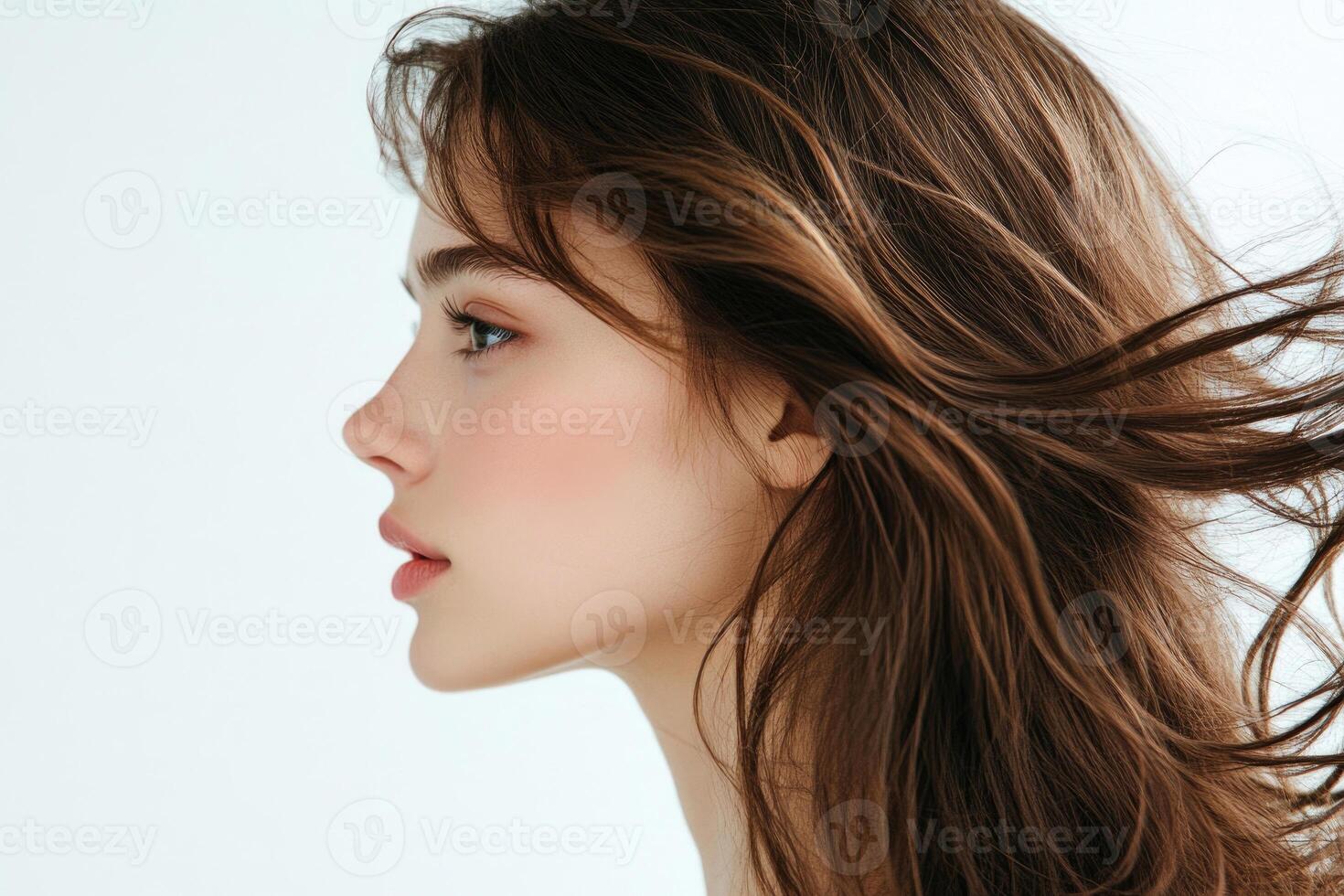 Profile shot of a beautiful young brunette with wind-swept hair against a white backdrop. photo