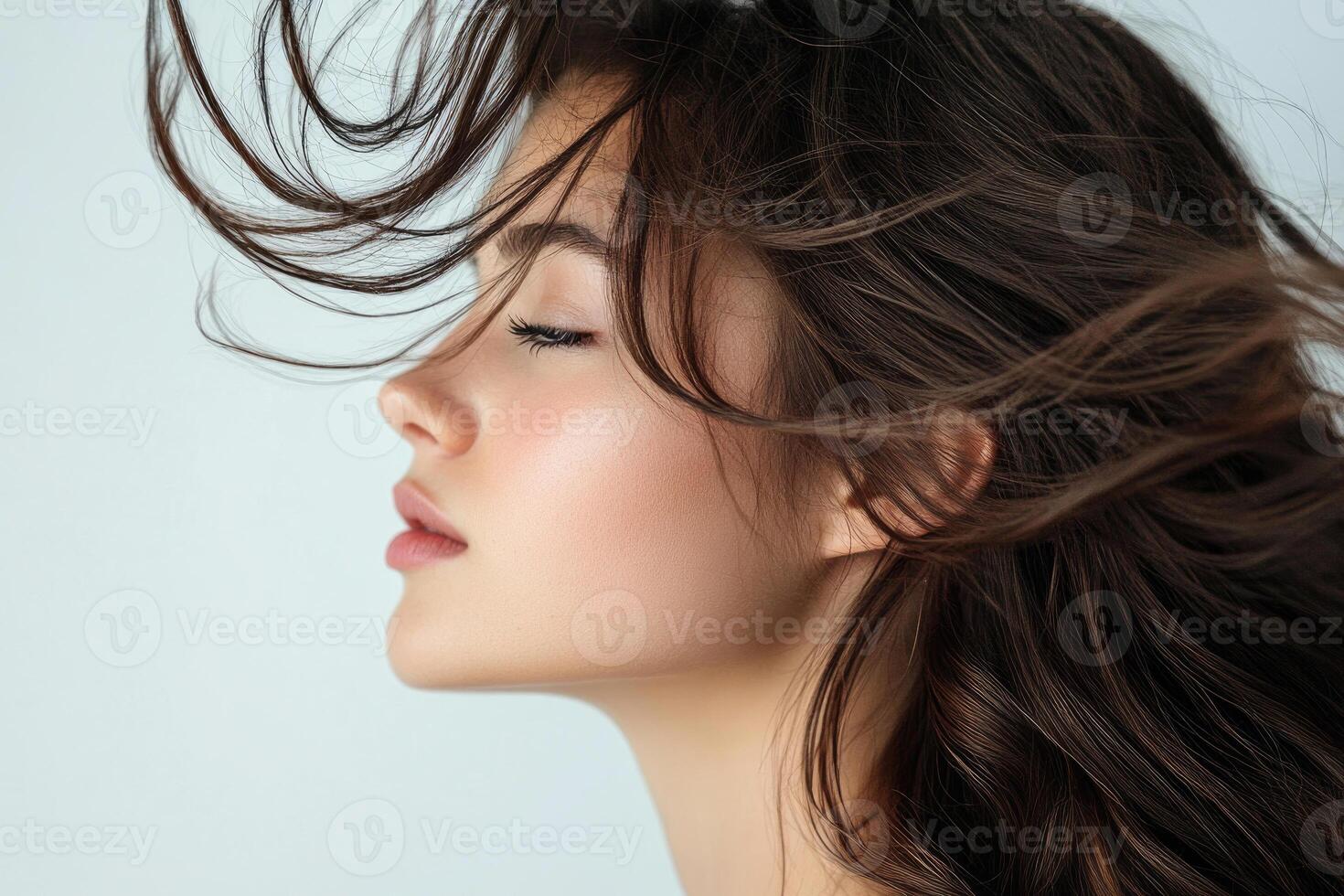 Profile shot of a beautiful young brunette with wind-swept hair against a white backdrop. photo