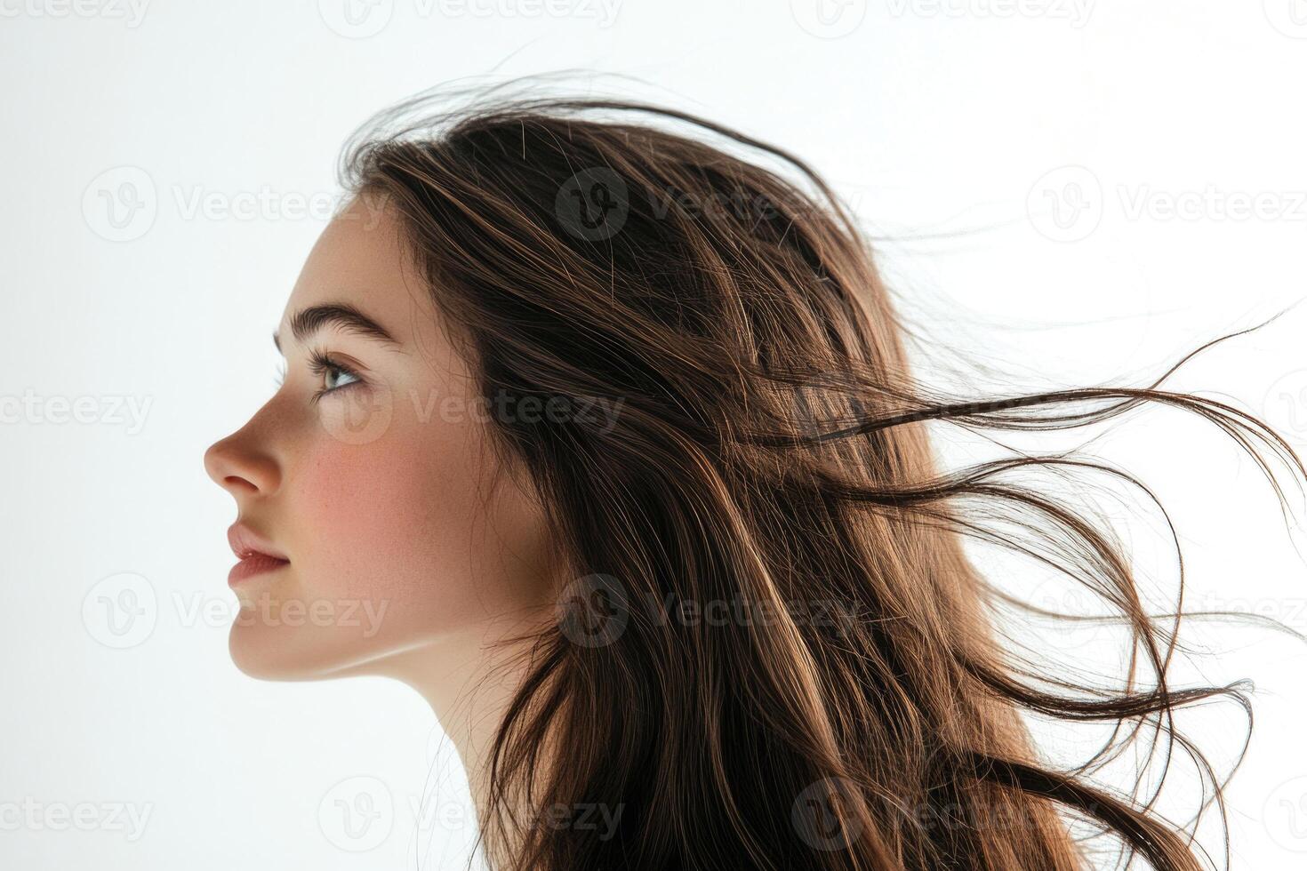 Profile shot of a beautiful young brunette with wind-swept hair against a white backdrop. photo