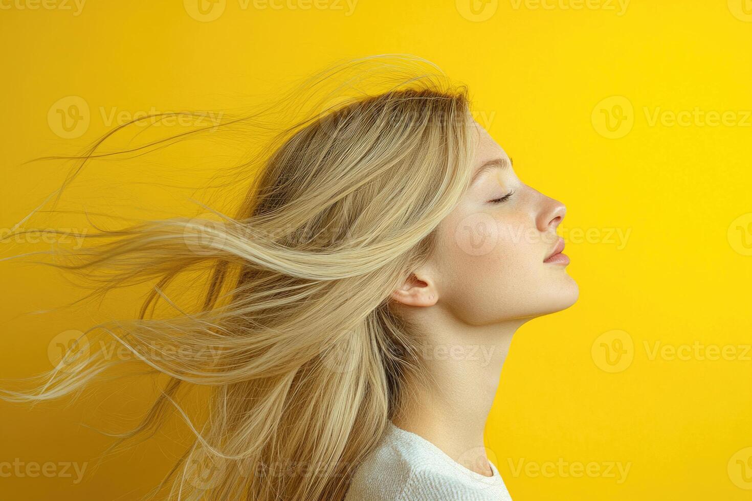 Profile portrait of a blonde woman with hair flowing in the wind on a yellow backdrop. photo