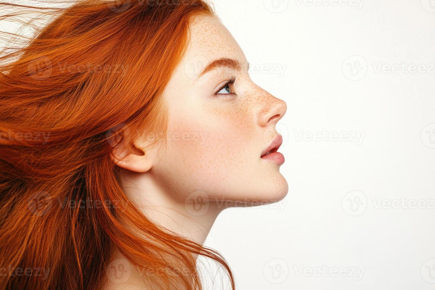 Profile portrait of a beautiful red-haired young woman with flowing hair on a white studio background. photo
