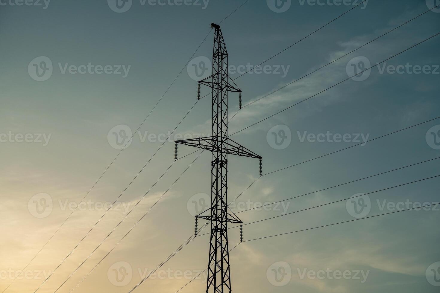 High voltage pole and wires against blue sky and setting sun. photo