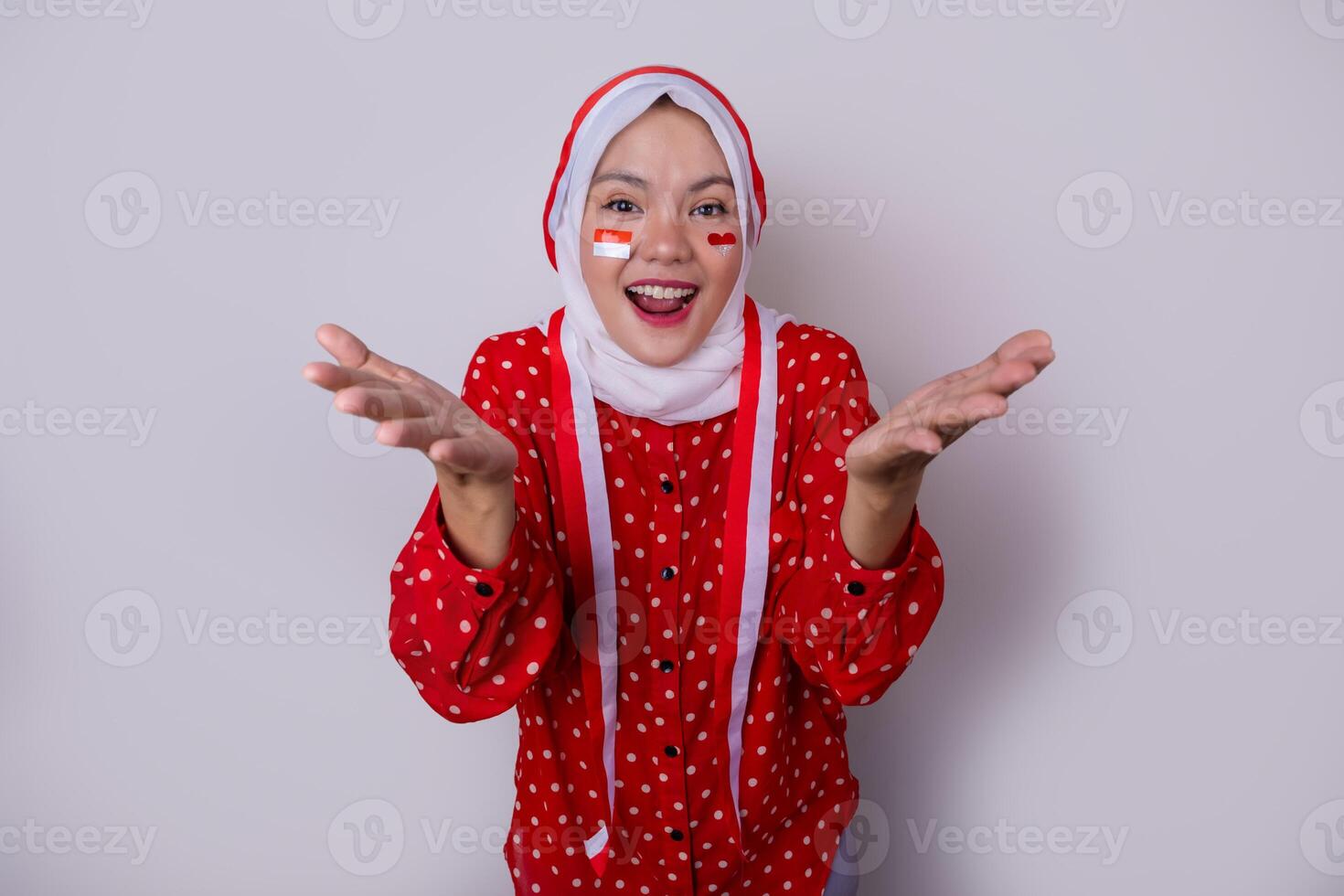 A hijab-wearing woman in a red outfit polkadot and an Indonesian flag headband poses in a celebration of Independence Day. The photo reflects patriotism and national pride.