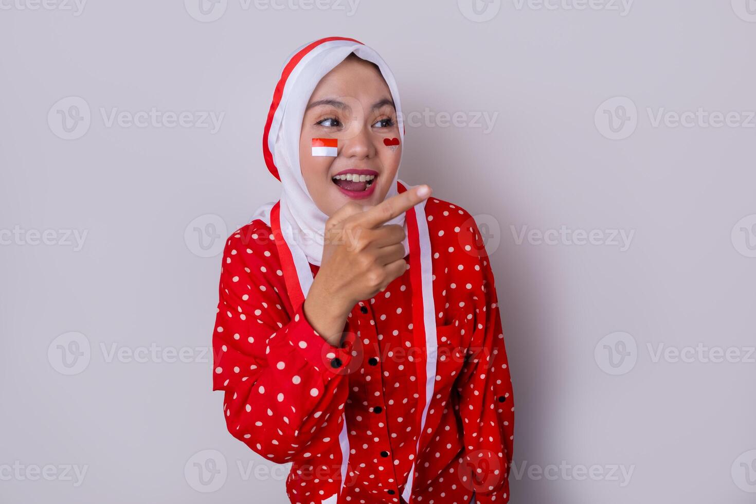 A hijab-wearing woman in a red outfit polkadot and an Indonesian flag headband poses in a celebration of Independence Day. The photo reflects patriotism and national pride.