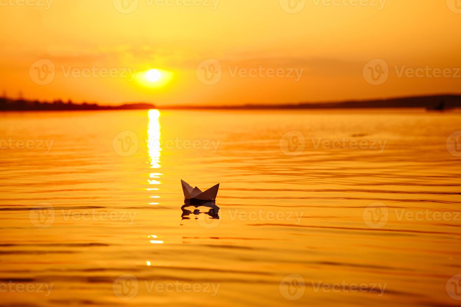 A paper boat floating away into the distance. Boat on the water. Beautiful sunset. Origami. River. Lake. photo