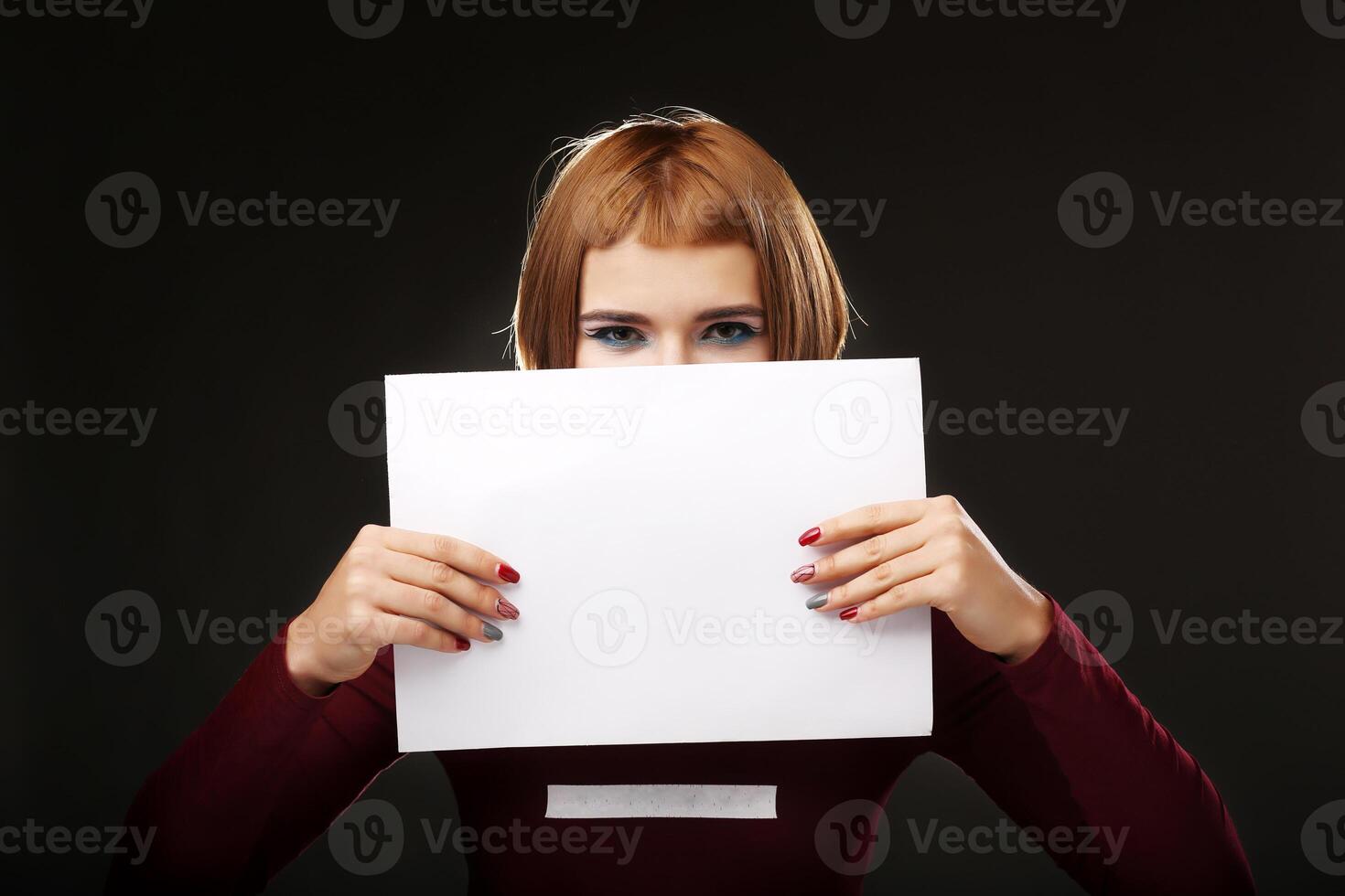 Young woman showing on empty blank board. Colorful studio portrait, isolated on black background. Space for text photo