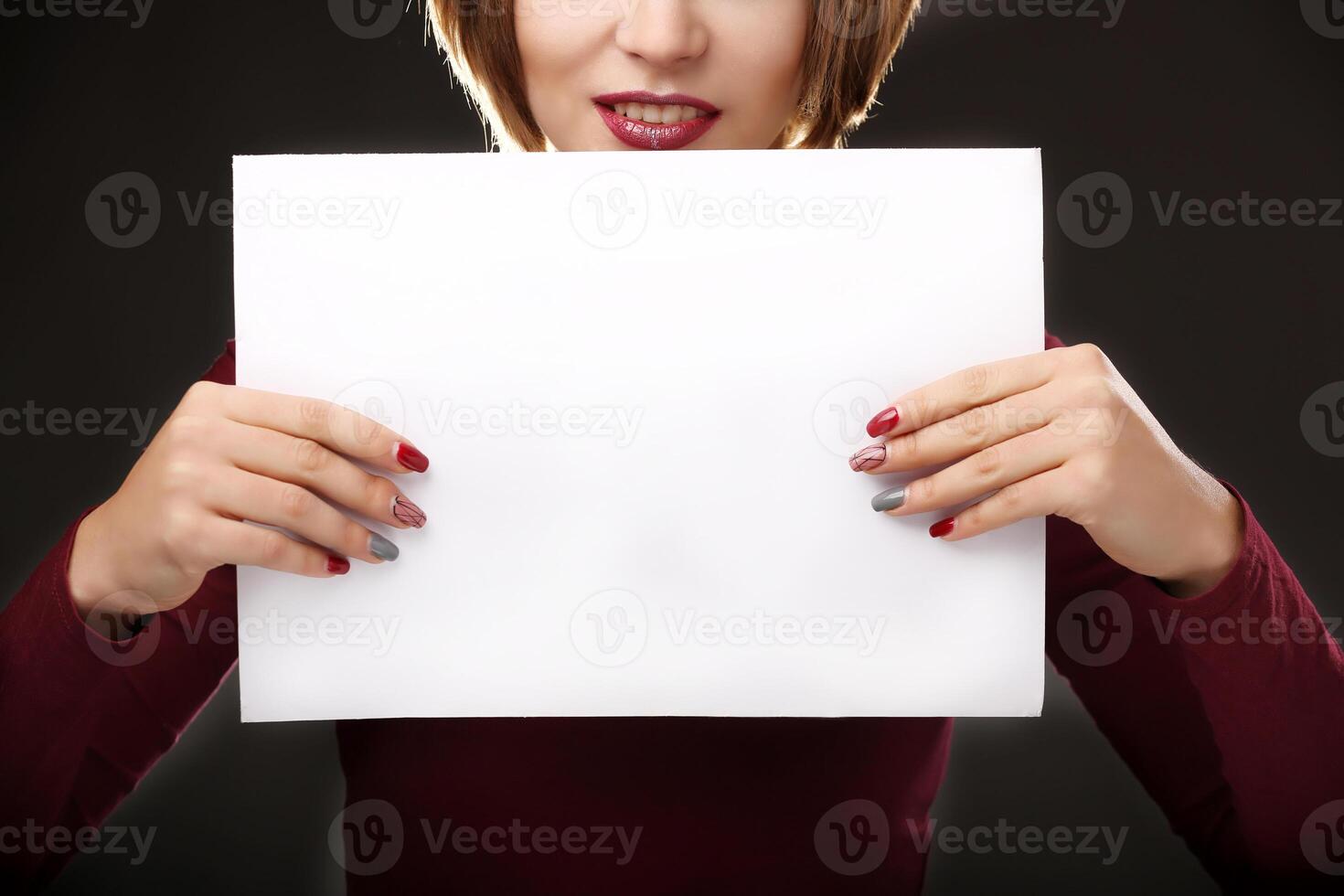 Red-haired woman holding an empty A4 card. Isolated on black background. Space for text photo