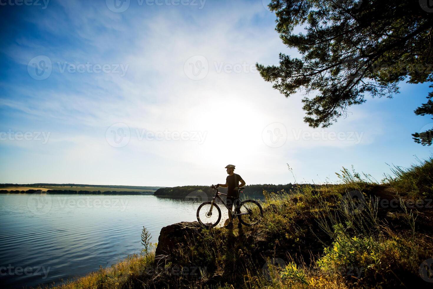 Side view of the rider on a bicycle standing on a rock and enjoying the sunset. Motivation and inspiration for adventure. photo
