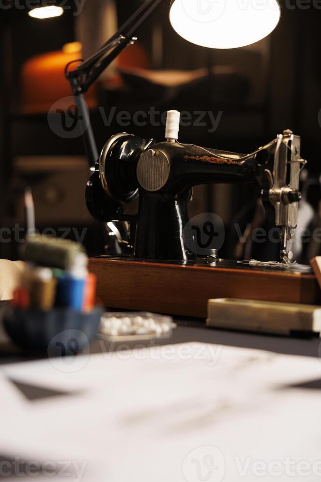 Focus on expensive industrial sewing machine in atelier shop used for embroidery and cutting textile fabrics. Professional tailoring studio workspace with sketch drawings and dressmaking instruments photo