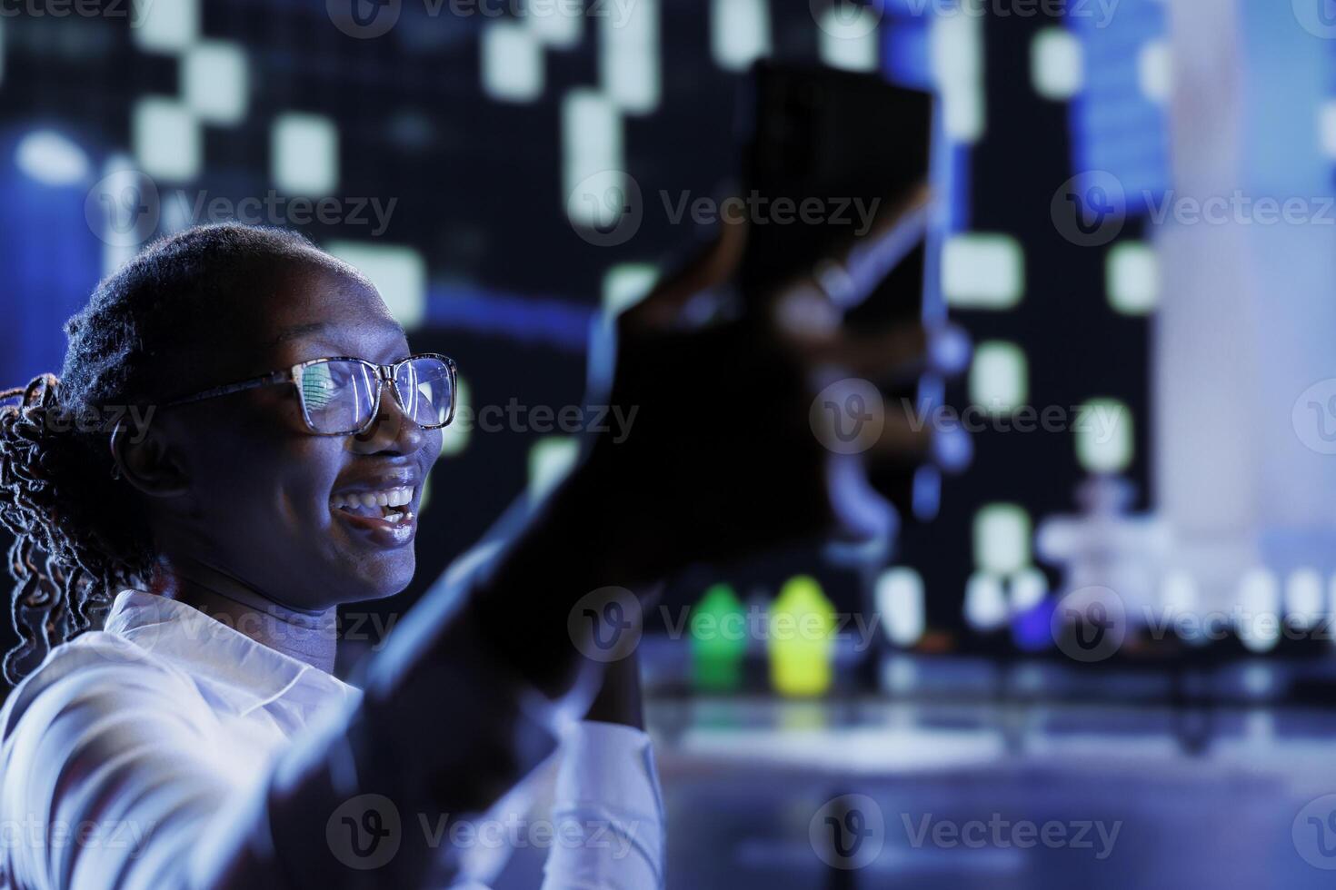 Woman making faces while using mobile phone to take selfie walking around city at night. Citizen using cellphone to take pictures of herself for social media while strolling outside on empty streets photo