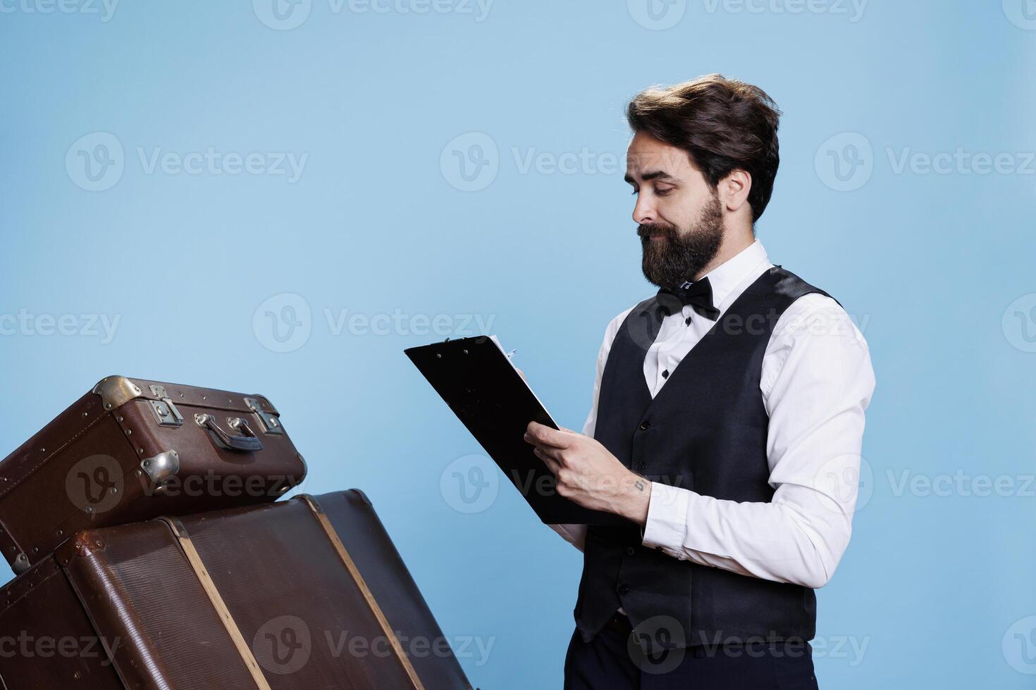 Bellhop reading checklist of tourists, holding catalogue register on clipboard to verify list of guests at hotel. Doorkeeper checking reservations on official log archive papers, take notes. photo