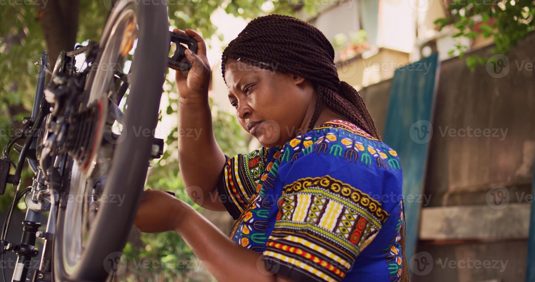 Sportloving african american female checking and securing bicycle wheel with specialized multitool in home yard. Active black woman using expert work tool to tighten bike cogset for safe cycling. photo