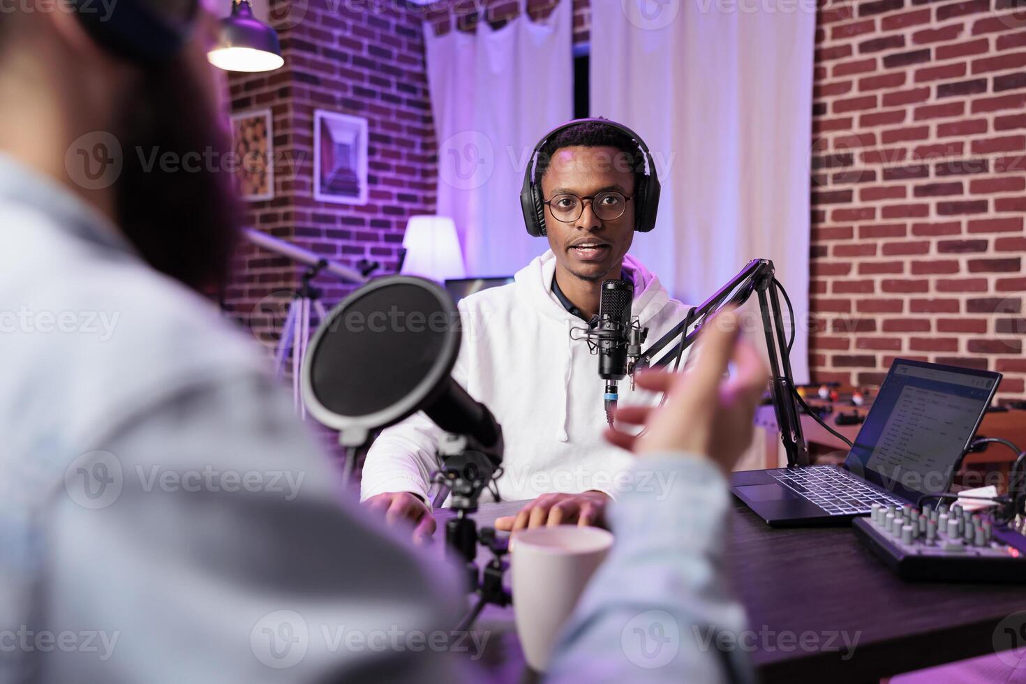 Interesting guest on online podcast show telling cool story to host, entertaining viewers watching during live broadcast. Presenter using audio recording equipment in living room studio photo