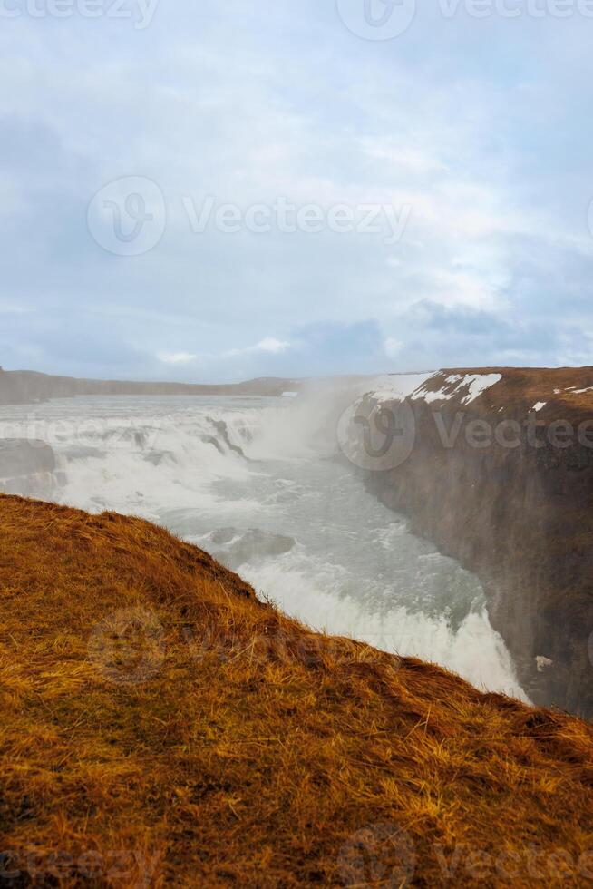 Large water flowing from hillsides and slopes in Iceland arctic Gulfoss cascade. Fabulous icelandic landscape with freezing river in nordic region falling off of cliffs, natural wilderness. photo