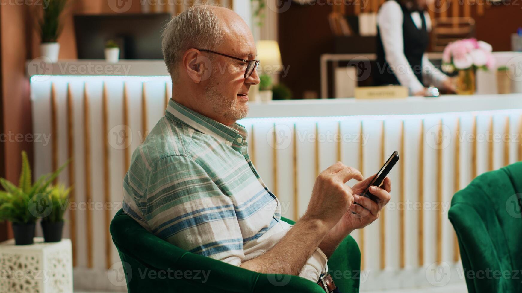 Retired man checking smartphone app in lounge area at five star hotel, using online browser to navigate on social media. Senior traveller relaxing in holiday retreat lobby. Handheld shot. photo