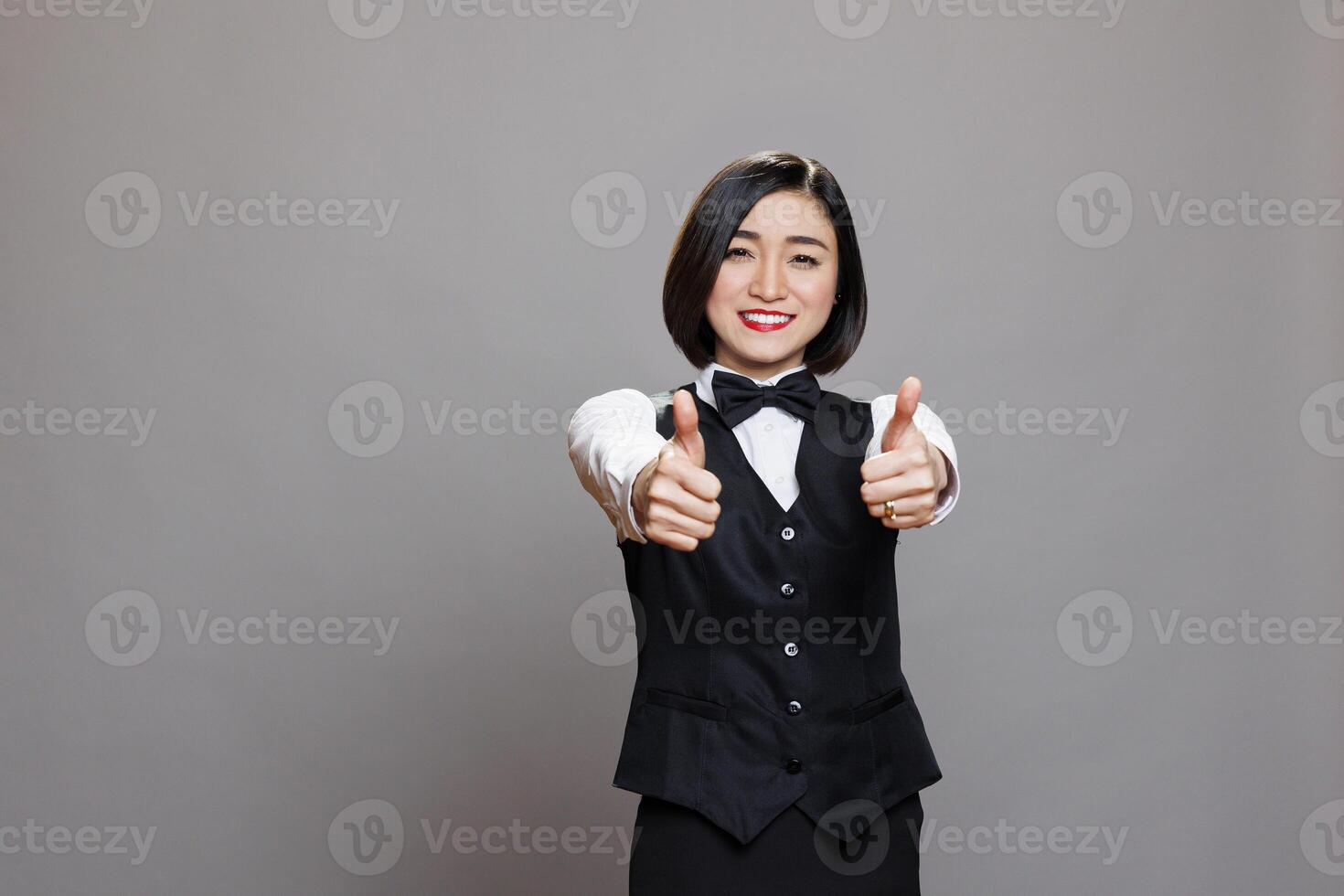 Smiling asian waitress with thumbs up recommending catering service portrait. Cheerful young attractive receptionist wearing restaurant uniform showing approval gesture and looking at camera photo
