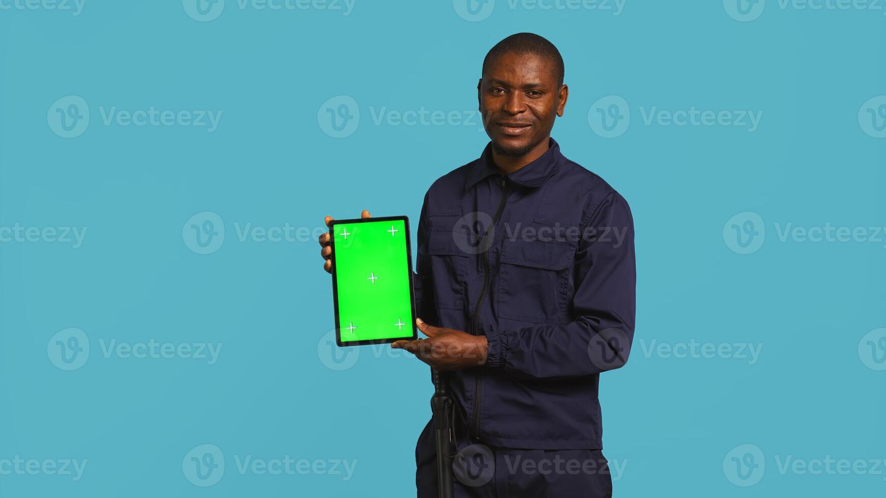 Portrait of smiling security guard at work showcasing isolated screen tablet while overseeing premises. Joyful private law enforcement worker presenting chroma key device, studio backdrop, camera B photo