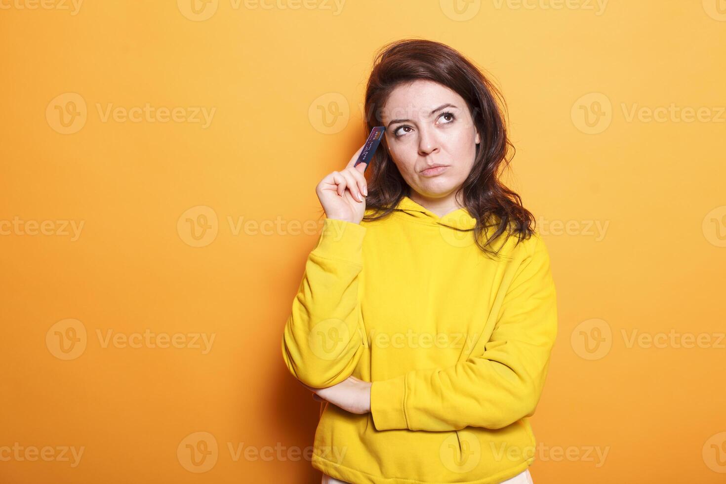 Young female individual grasping debit card and contemplating purchase. Thoughtful caucasian woman preparing to shop online using her money and internet banking. photo
