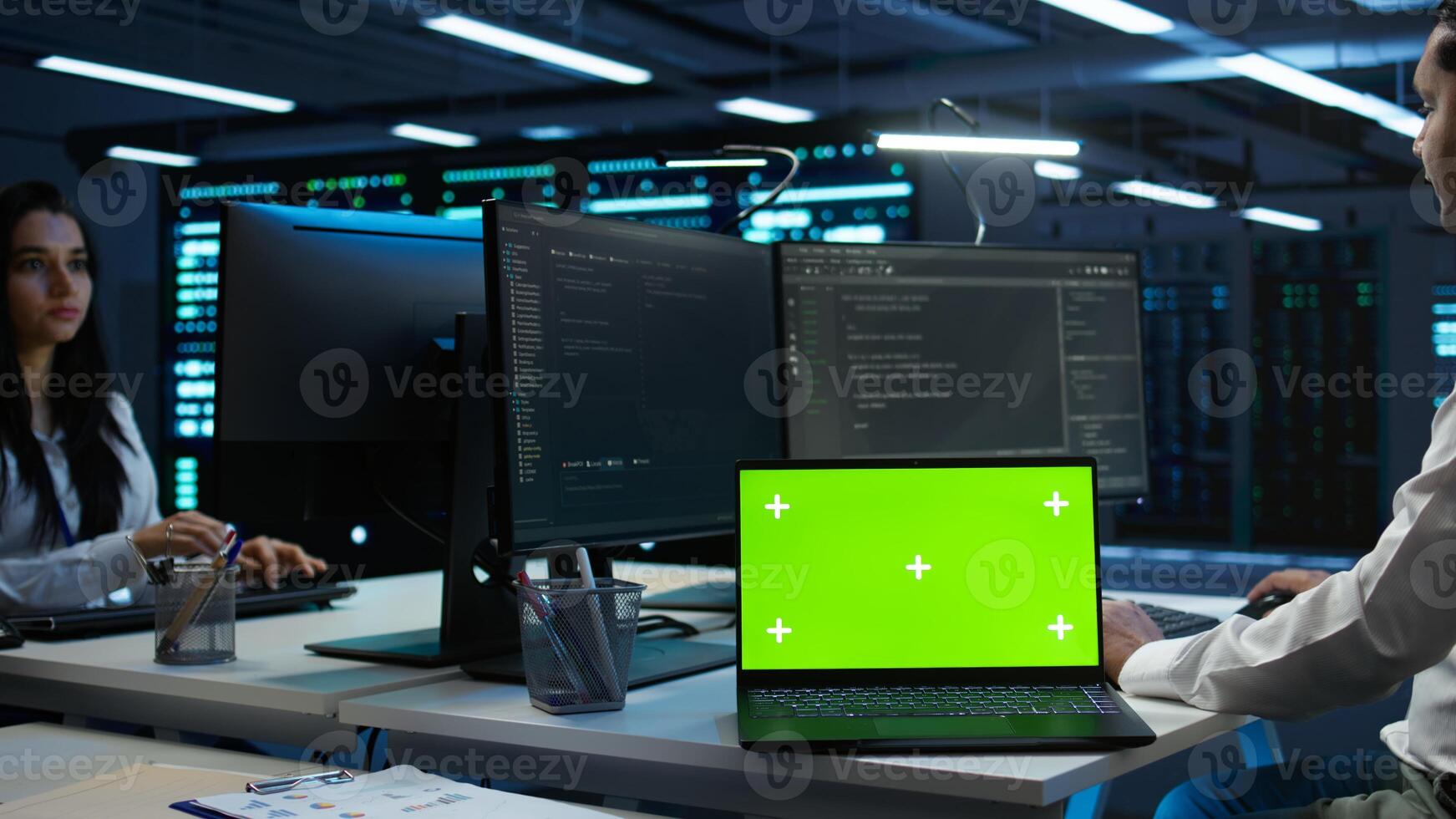 Zoom in on green screen laptop used by data center worker troubleshooting issues. Engineer uses chroma key notebook in server hub, establishing performance benchmarks, camera B photo