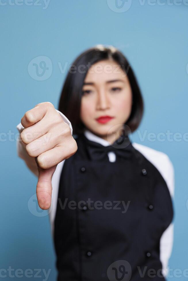 Dissatisfied asian waitress showing thumb down sign, expressing negative feedback and disapproval portrait. Receptionist displaying bad service experience concept and looking at camera photo