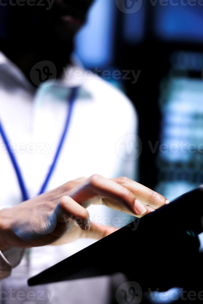 Close up shot of employee running data center hardware diagnostic tests to determine and service software issues. African american repairman using tablet to fix critical systems, checking for blips photo