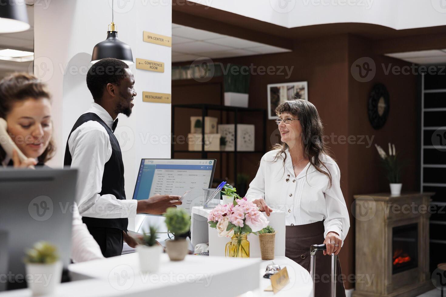 Senior woman at front desk assisted by employee with check-in, verifying identification in hotel reception. Male concierge completes registration process for elderly female traveler with her passport. photo