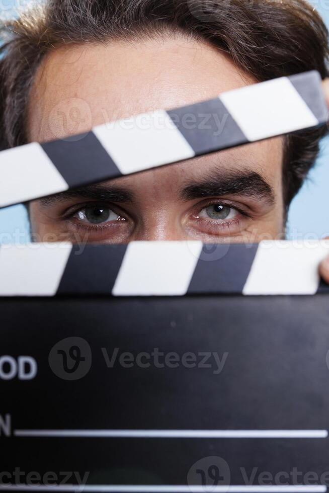 Hotel porter poses with filmslate on set to cut scenes and say action, using accessory for post production movie industry. Young man holding clapperboard for filming, studio background. Close up. photo