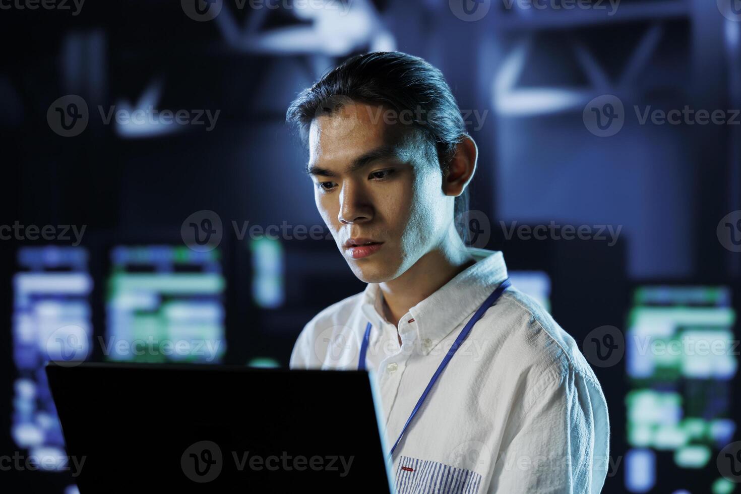 Dara center tech support running code and programming on laptop, troubleshooting and upgrading high tech facility designed to accommodate rows of fully operational server rackmounts photo
