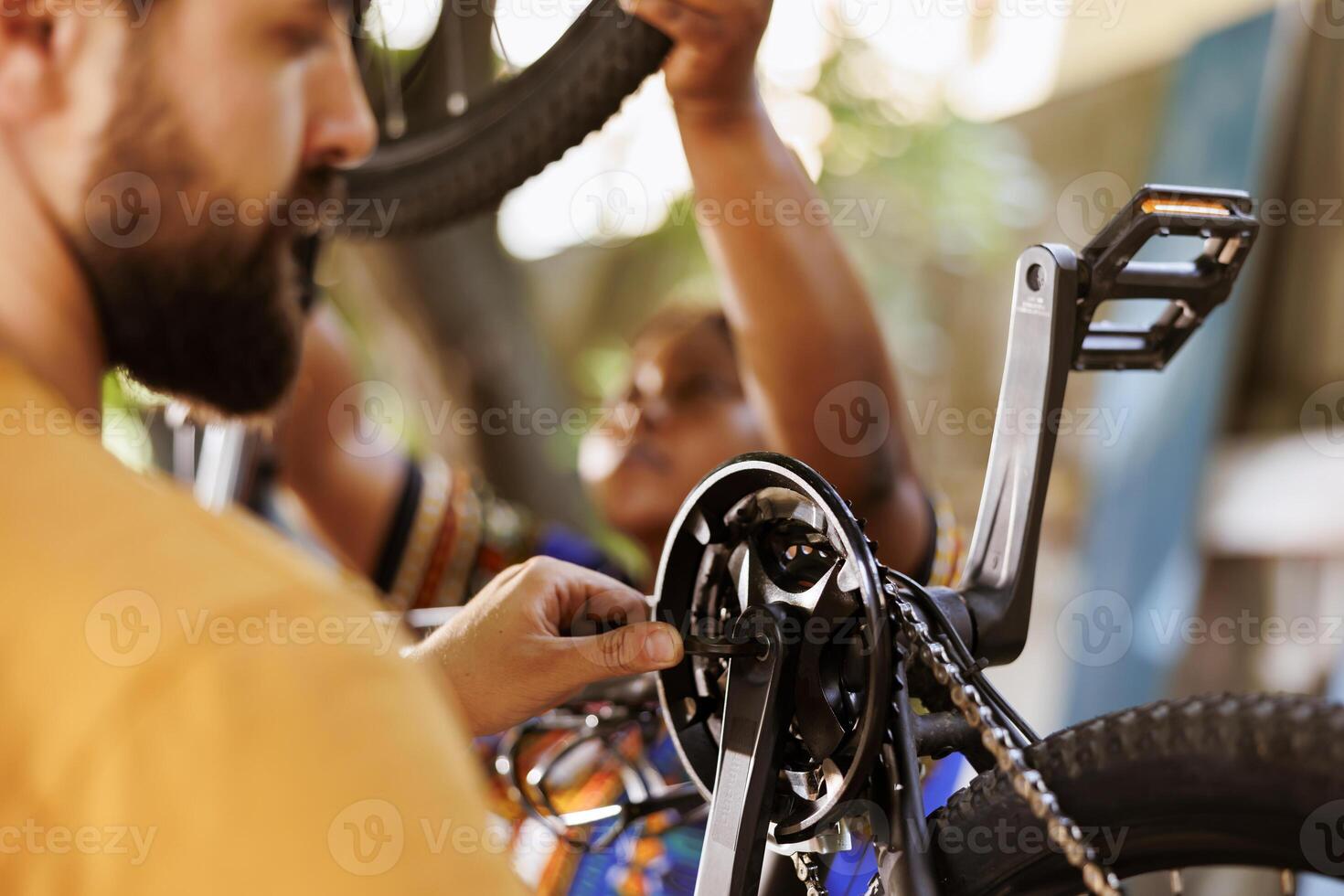 Close up of active dedicated young man adjusting bike derailleur with professional equipment in home yard. Healthy male cyclist securing and tightening bicycle chain with allen key tool. photo