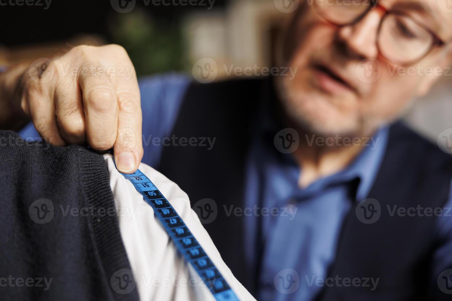 Extreme close up of blue measurement tape on elegant customer shoulder during garment fitting process. Elderly professional meticulous suitmaker honoring client sartorial comission photo
