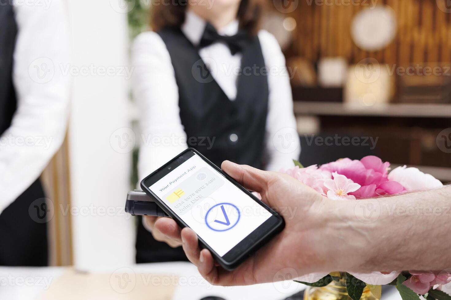 Close-up shot of caucasian old man making payment transaction using mobile phone at registration counter. Detailed view of a person using smartphone to pay for check-in reservation at hotel reception. photo