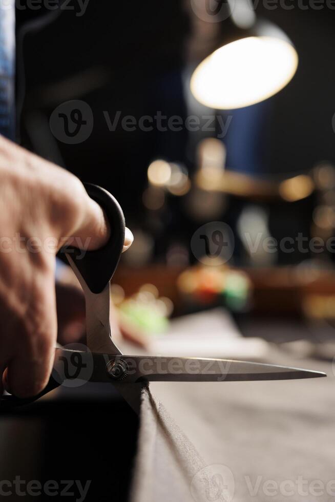 Skillful craftsman using scissors to cut refined fabric material in tailoring studio, making premium quality sartorial collection. Precise suitmaker handcrafting bespoke business suit piece, close up photo