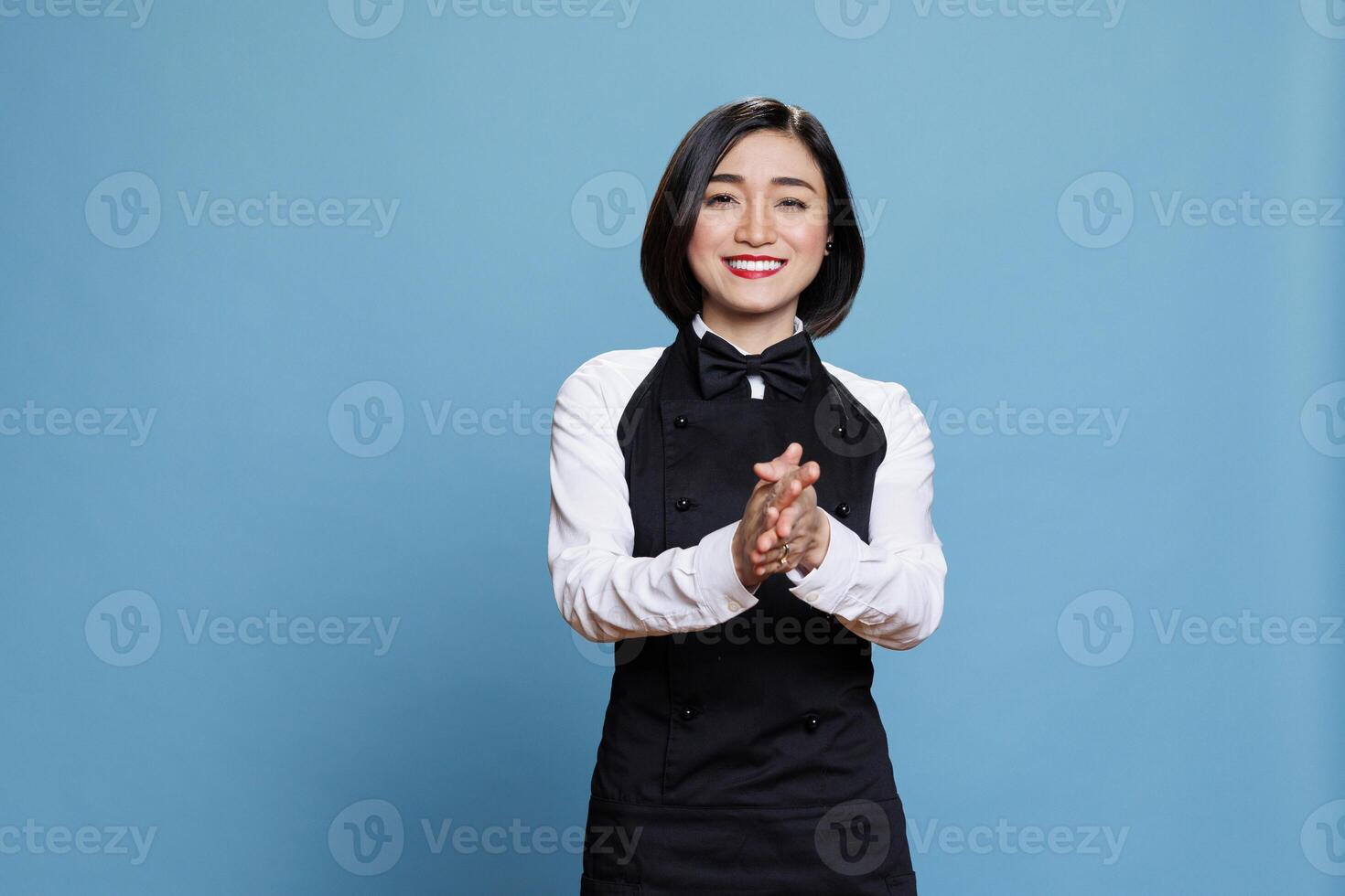 Smiling asian waitress wearing uniform applauding with to show support and appreciation portrait. Cheerful young attractive woman receptionist clapping hands and looking at camera photo