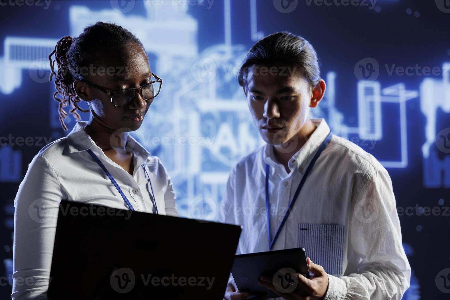 BIPOC coworkers updating neural networks, writing intricate binary code scripts on laptop and tablet. Teamworking colleagues using programming to upgrade AI simulation model photo