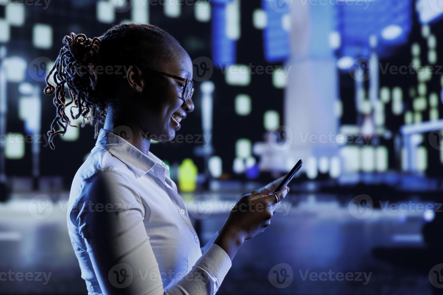 BIPOC woman walking around city at night, scrolling on online shopping platform using mobile phone. Citizen using smartphone while strolling outside on empty streets illuminated by lamps photo