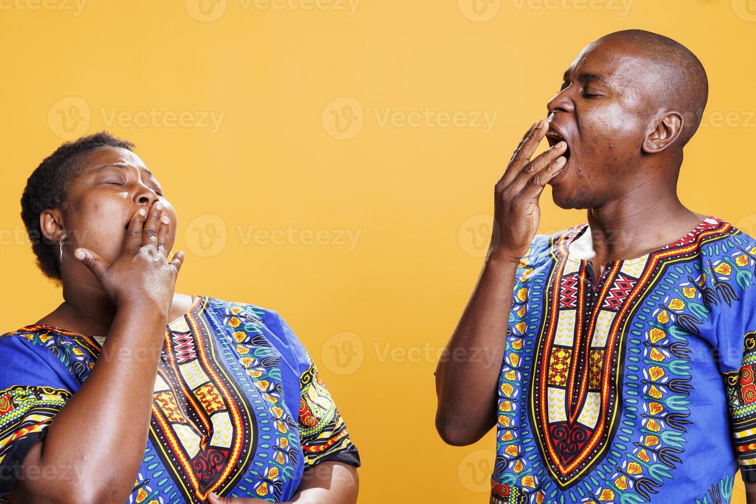 Tired black man and woman pair yawning and covering mouth with hand. Exhausted african american couple showing lack of sleep gesture and feeling fatigue in morning in studio photo