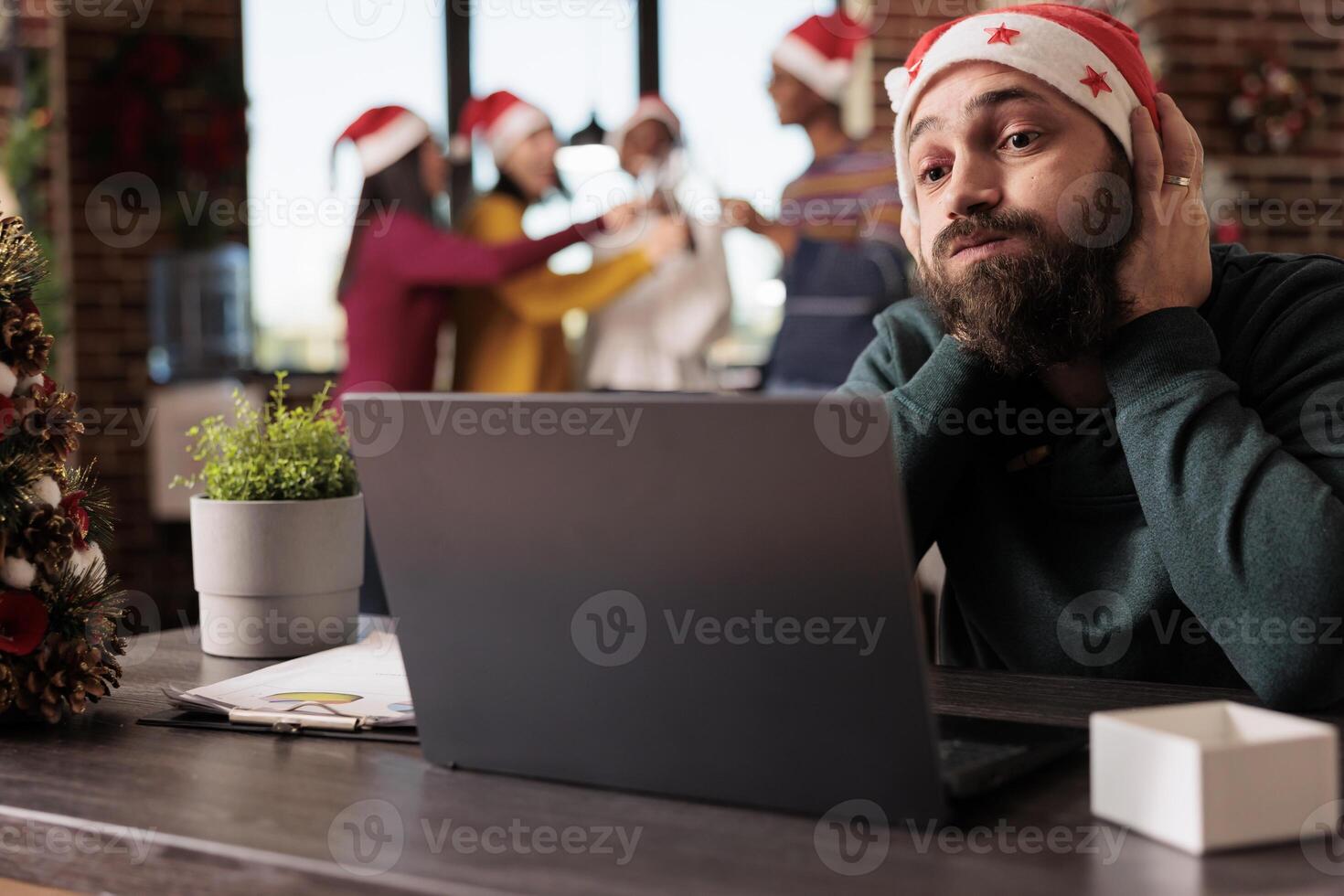 Stressed tired company worker having burnout while managing workload on laptop in xmas decorated office. Exhausted caucasian man in santa hat sitting at workplace during new year holiday photo
