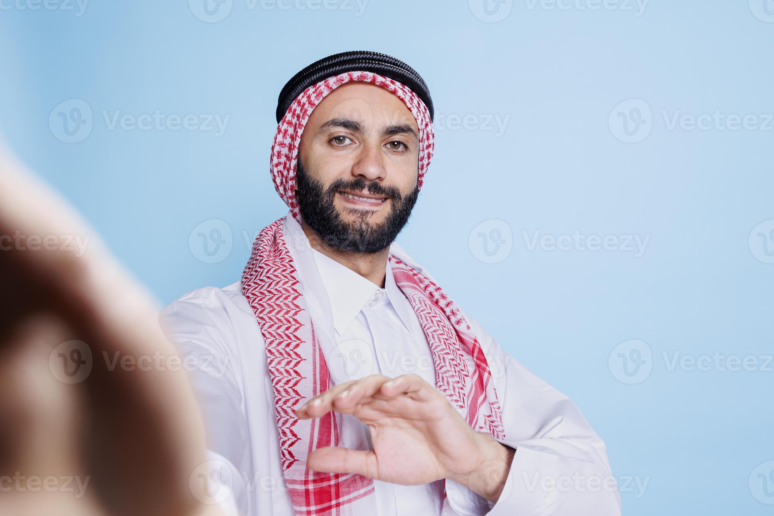 Smiling arab man wearing traditional attire holding mobile phone in arm and  looking at front camera fpv. Muslim person with cheerful expression talking  in videocall pov perspective 49011218 Stock Photo at Vecteezy