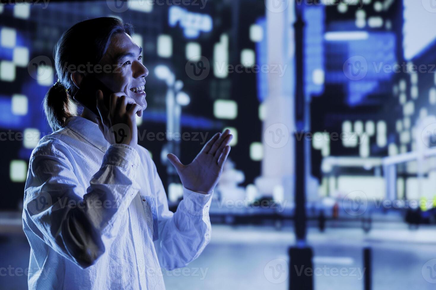 Happy man strolling around cityscape during nighttime, enjoying discussion over the phone with girlfriend. Asian citizen walking home from work, making telephone calls while commuting photo