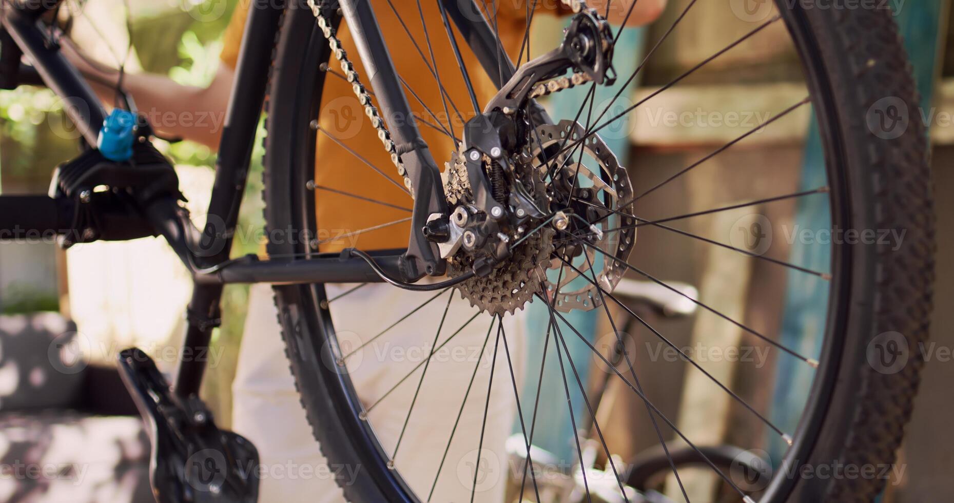 Different bike components including the rear derailleur pulley wheel and cassette seen up close being maintained outside. Caucasian man thoroughly inspecting and securing bicycle tire. photo