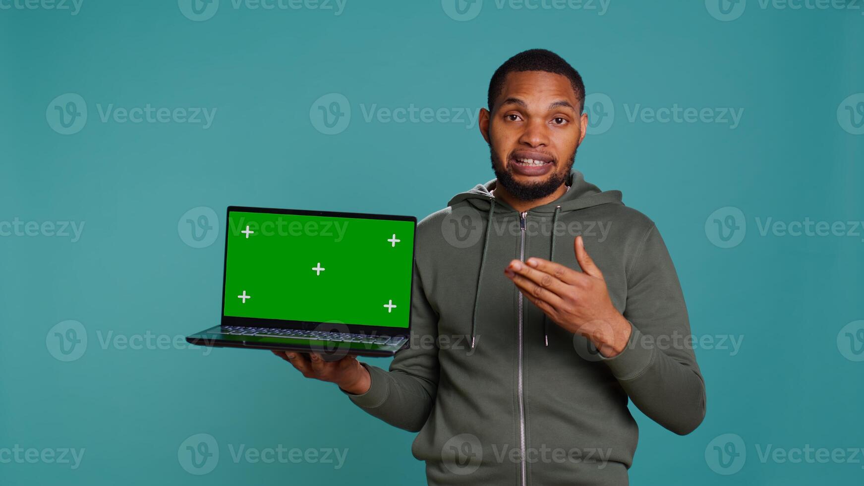 Smiling man holding isolated screen laptop, doing recommendation, talking with audience. Cheerful person pointing towards chroma key notebook, studio background, camera B photo