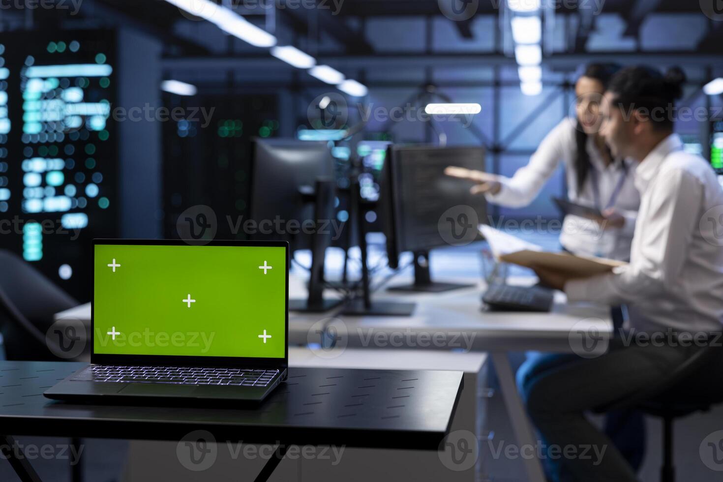 Close up of green screen laptop in data center with workers checking emergency procedures documents. Focus on chroma key notebook in front of server hub employees in blurry background photo