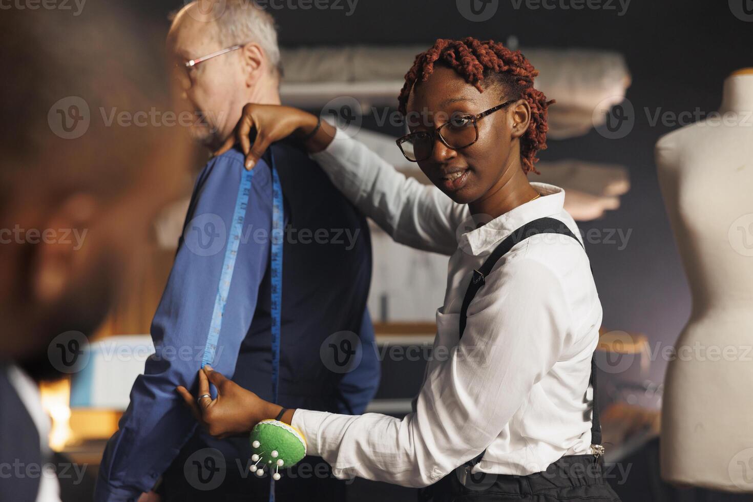 African american needleworker providing arm measurements to suitmaking craftsman in sartorial process. Skilled seamstress using tape to determine proper business suit sleave length photo