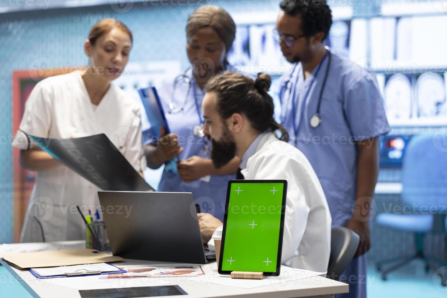 Team of doctors consulting analytics next to green screen on laptop in medical cabinet, examining x ray scan results to find the diagnosis. Licensed medics review hospital records at desk. photo