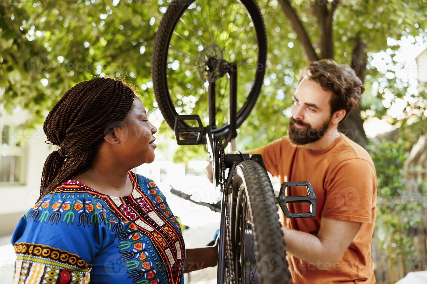 Eager sportloving multiracial couple inspecting bicycle gear to use for yearly summer hobby activity. At home yard, active boyfriend and girlfriend doing bike maintenance for leisure cycling. photo