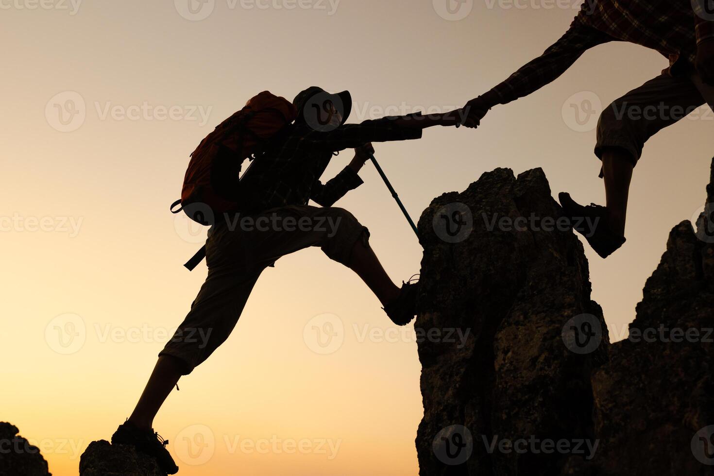 Silhouette of two climbers reaching out for help on a rocky ridge at sunrise over a valley, Success, teamwork and unity. photo