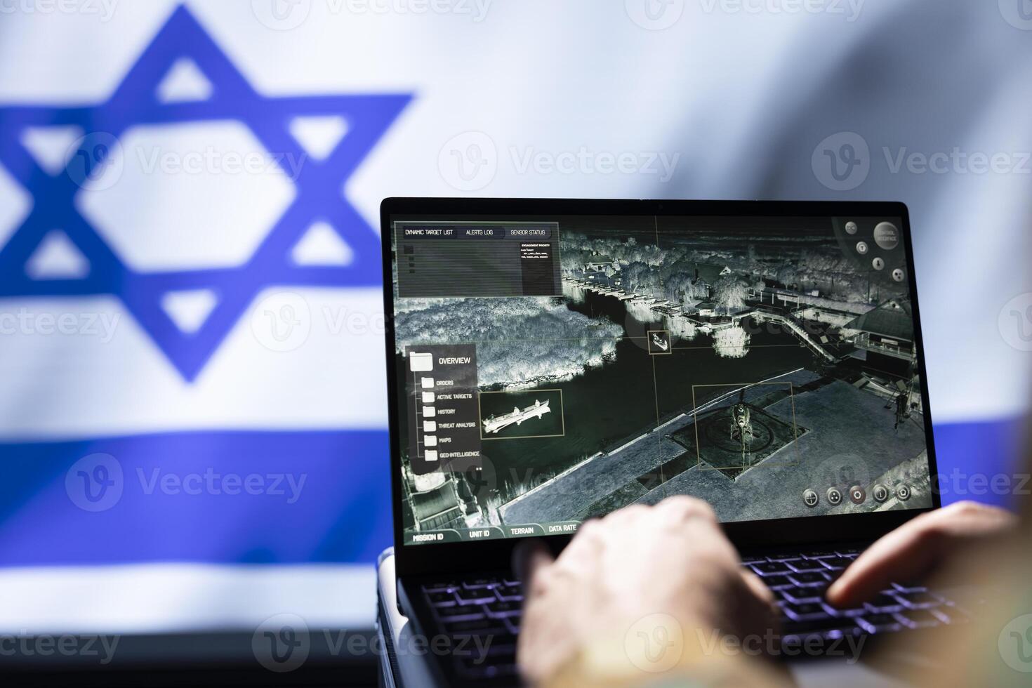 Israel Defense Forces military operative uses laptop to analyze surveillance data, standing isolated over Israeli flag background. Close up of soldier engaged in Middle Eastern geopolitical operation photo