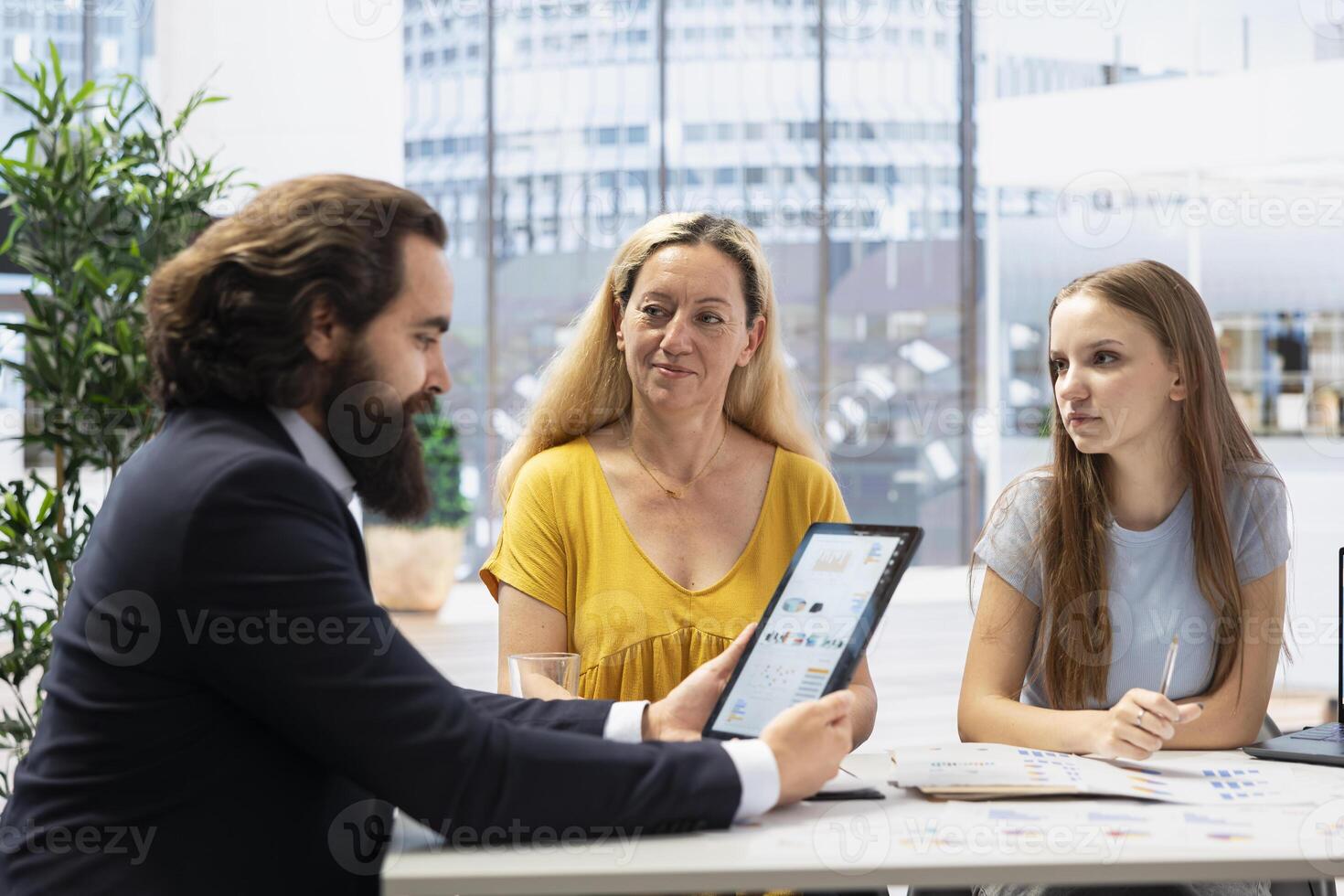 Financial advisor creating reports and statistic charts on investment performance on tablet, showing them to clients. Agent using device to develop portfolio diagram graphs for customers photo